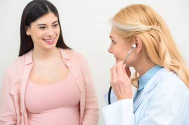 close-up shot of obstetrician gynecologist listening heartbeat of child fetus of pregnant woman with stethoscope