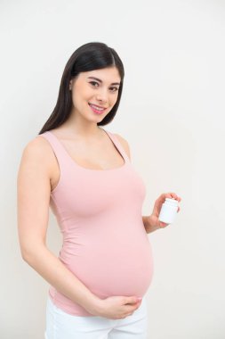happy young pregnant woman holding jar of pills on white clipart
