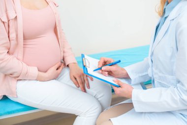 cropped shot of obstetrician gynecologist consulting pregnant woman at clinic clipart