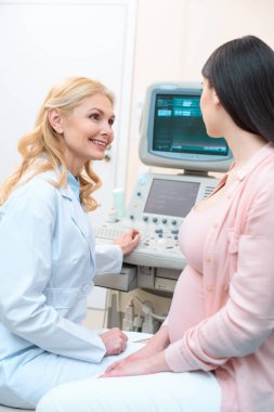 obstetrician gynecologist showing ultrasonic equipment to pregnant woman clipart