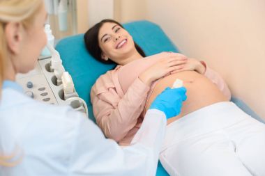 obstetrician gynecologist making ultrasound examination for young pregnant woman clipart