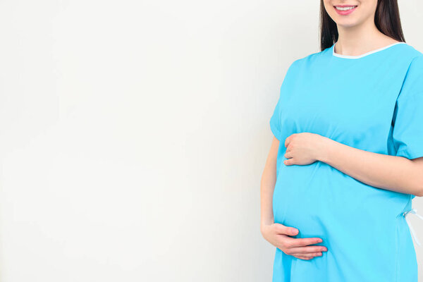 cropped shot of pregnant woman in medical coat touching her belly on white