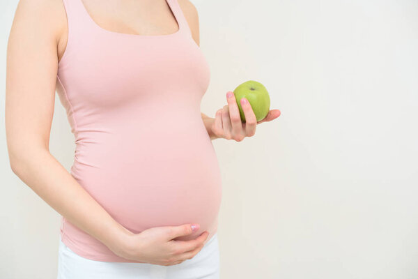 cropped shot of pregnant woman with green apple on white