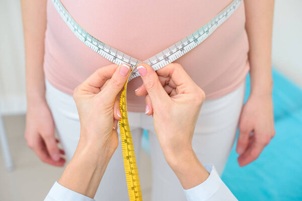 cropped shot of female obstetrician gynecologist measuring belly size of pregnant woman with measuring tape