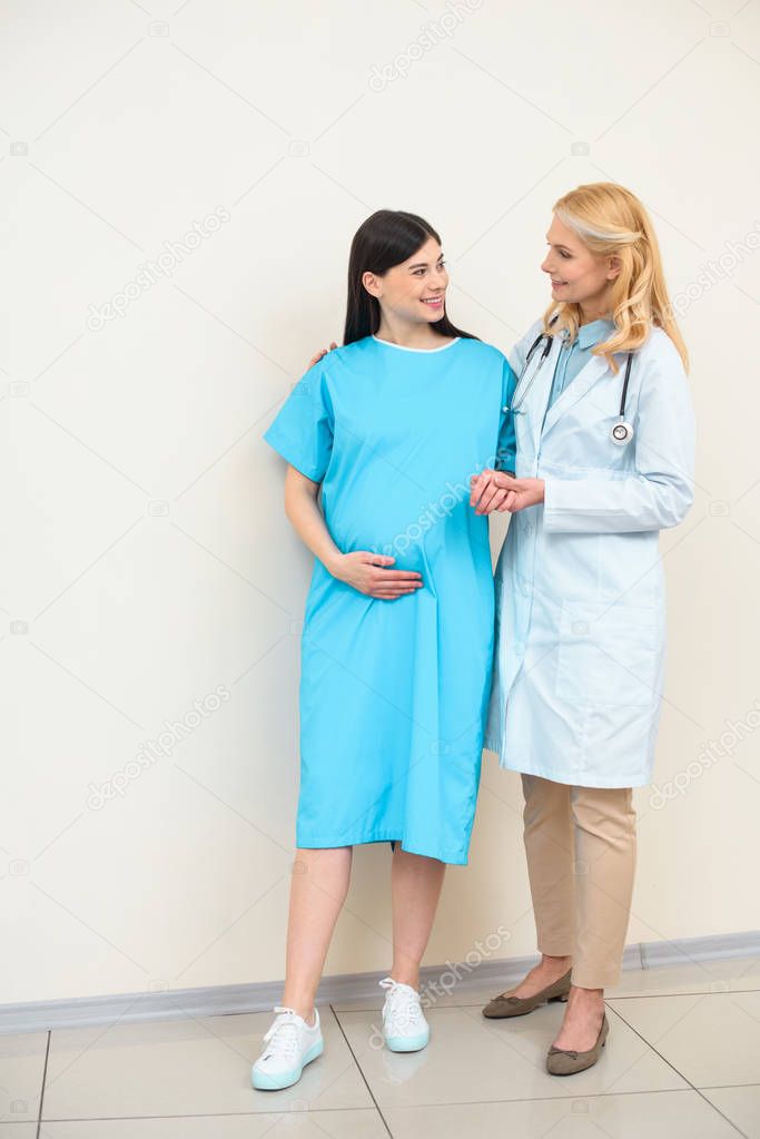 mature obstetrician gynecologist helping pregnant woman to walk and holding her hand