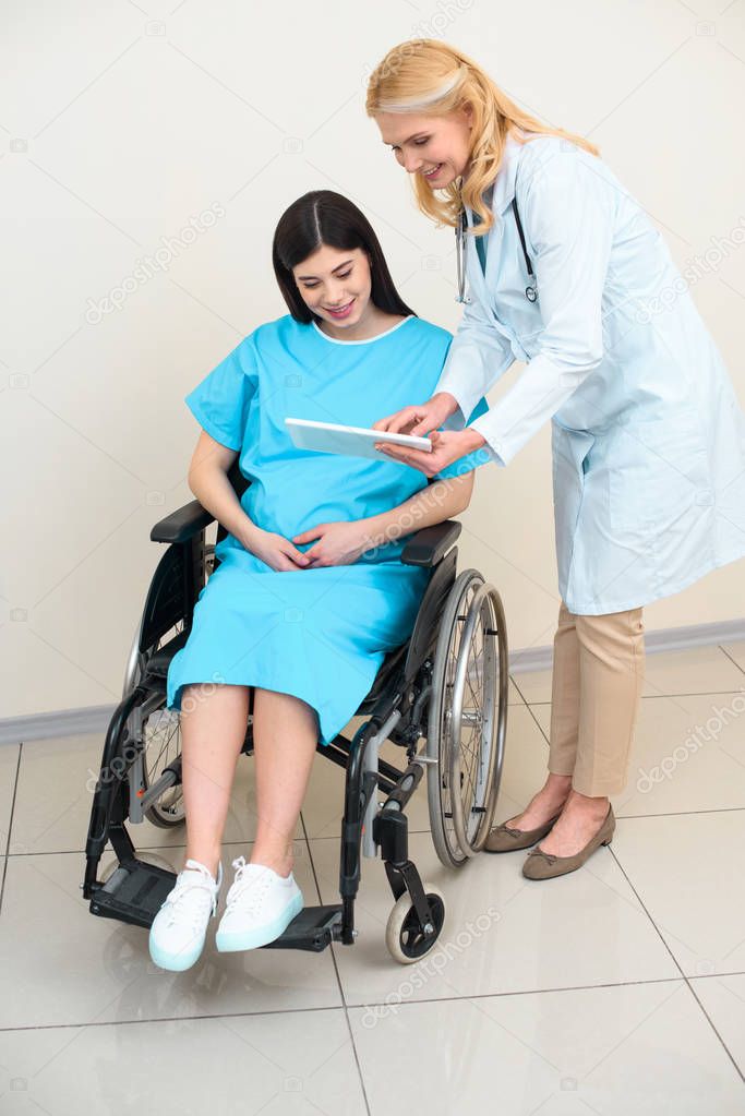 obstetrician gynecologist showing digital tablet to pregnant woman on wheelchair