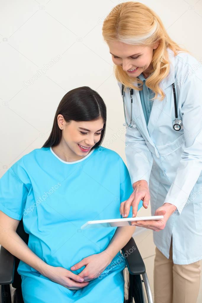 obstetrician gynecologist showing digital tablet to pregnant woman on wheelchair