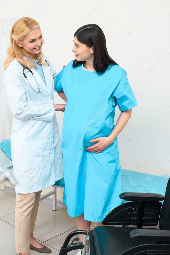 smiling obstetrician gynecologist helping pregnant woman to get to wheelchair
