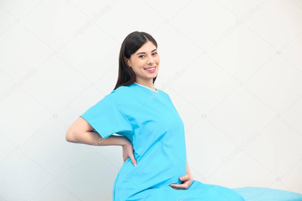 happy young pregnant woman sitting on bed at maternity hospital