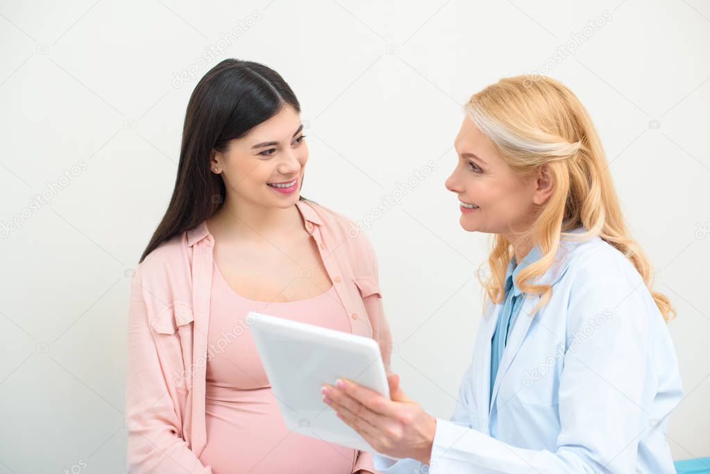mature obstetrician gynecologist and pregnant woman using tablet together
