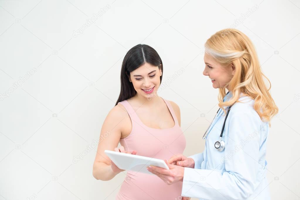 smiling obstetrician gynecologist and pregnant woman using tablet together