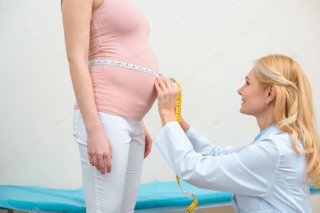 side view of obstetrician gynecologist measuring belly size of pregnant woman with measuring tape