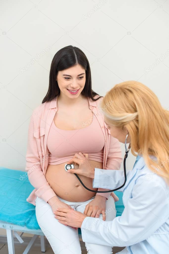 obstetrician gynecologist listening heartbeat of child fetus of happy pregnant woman with stethoscope