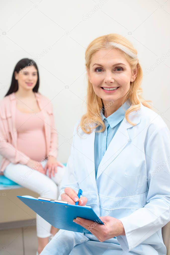 obstetrician gynecologist with clipboard and young pregnant woman blurred on background