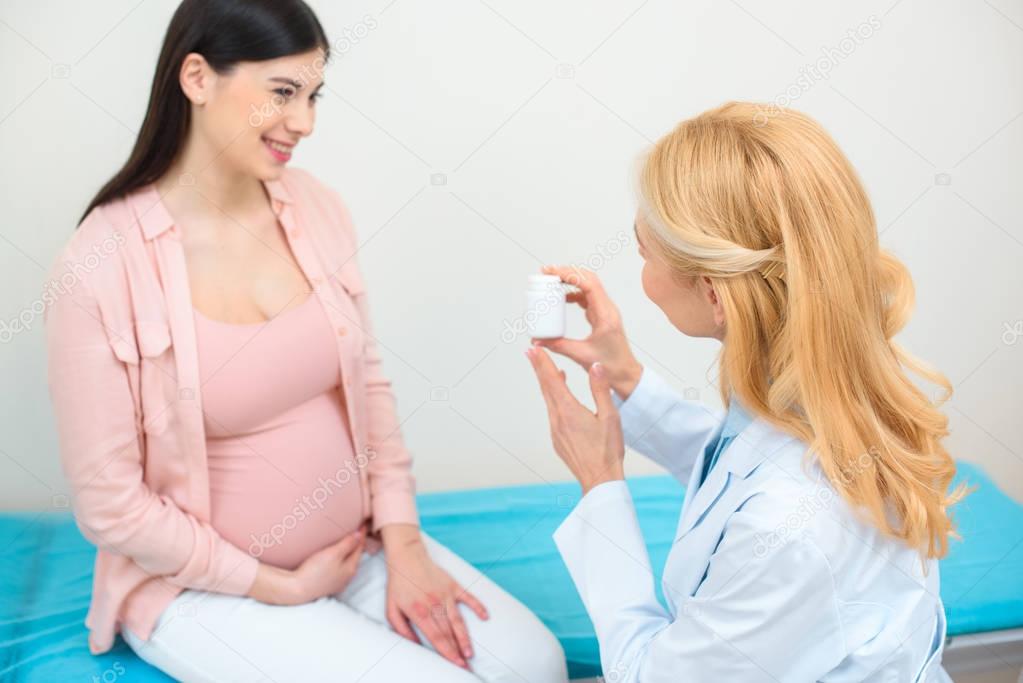 mature obstetrician gynecologist showing jar of pills to pregnant woman