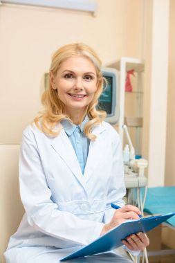 smiling obstetrician gynecologist writing in clipboard at ultrasonic office clipart