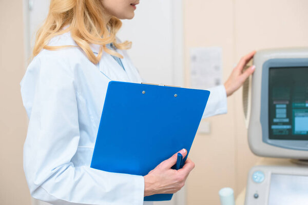 cropped shot of doctor with clipboard touching ultrasonic scanner