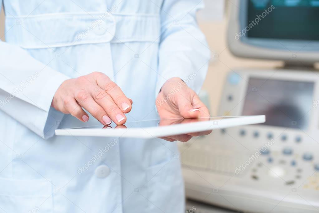 cropped shot of obstetrician gynecologist using tablet with ultrasonic scanner on background