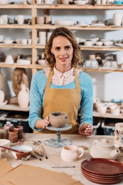 happy female potter decorating ceramic bowl in workshop  clipart