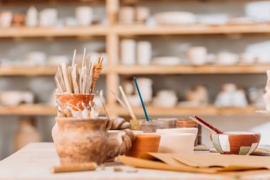selective focus of ceramics and pottery tools on wooden table in workshop clipart