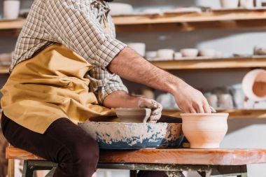 cropped view of potter making ceramic pots on pottery wheel in workshop clipart