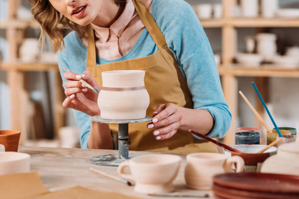 cropped view of woman painting ceramic jug in pottery workshop