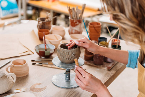 cropped view of woman decorating ceramic bowl in pottery workshop 