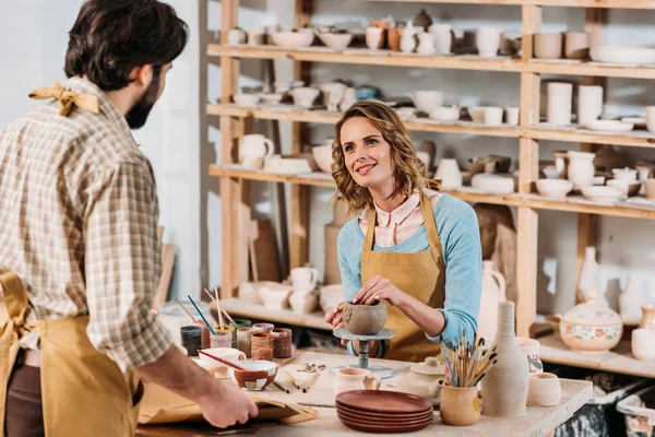 man with papers and female potter with ceramics in workshop