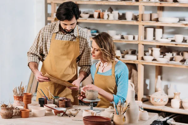 Paar Pottenbakkers Met Papieren Keramiek Verf Borstels Werkplaats — Stockfoto