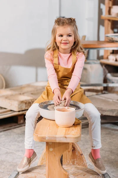 blonde smiling kid making ceramics on pottery wheel in workshop