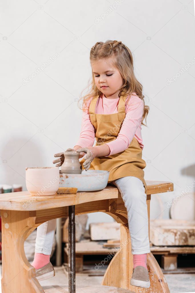 blonde child making ceramic pot on pottery wheel in workshop