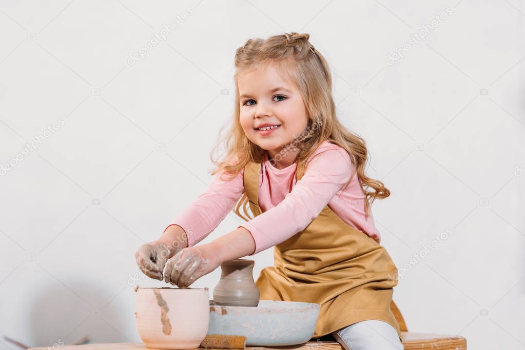 blonde smiling child making ceramic pot on pottery wheel in workshop