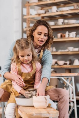 mother and daughter making ceramic pot on pottery wheel together clipart