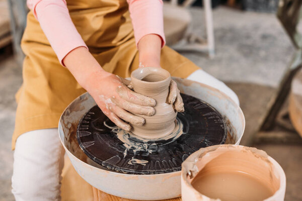 cropped view of kid making ceramic pot on pottery wheel in workshop