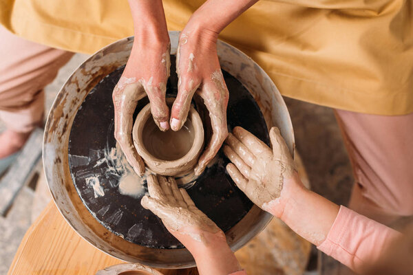 top view of teacher and kid making ceramic pot on pottery wheel