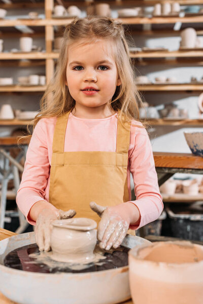 little child making ceramic pot with clay on pottery wheel in workshop