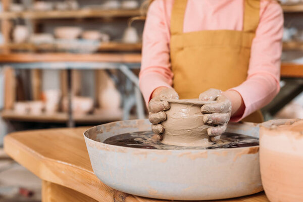 partial view of child making ceramic pot on pottery wheel in workshop