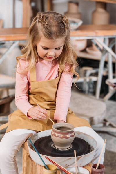 adorable blonde kid painting ceramic pot in workshop