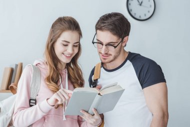sırt çantaları ile ayakta ve kitap okuma öğrenciler gülümseyen