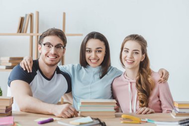 Kitaplar ile masada oturan öğrenciler gülümseyen genç  