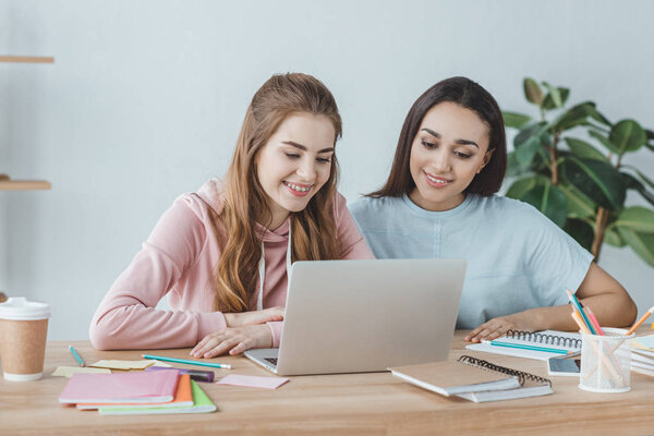 attractive multiethnic students using laptop at table with books  