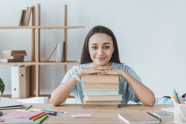 smiling mixed race girl sitting at table with books 