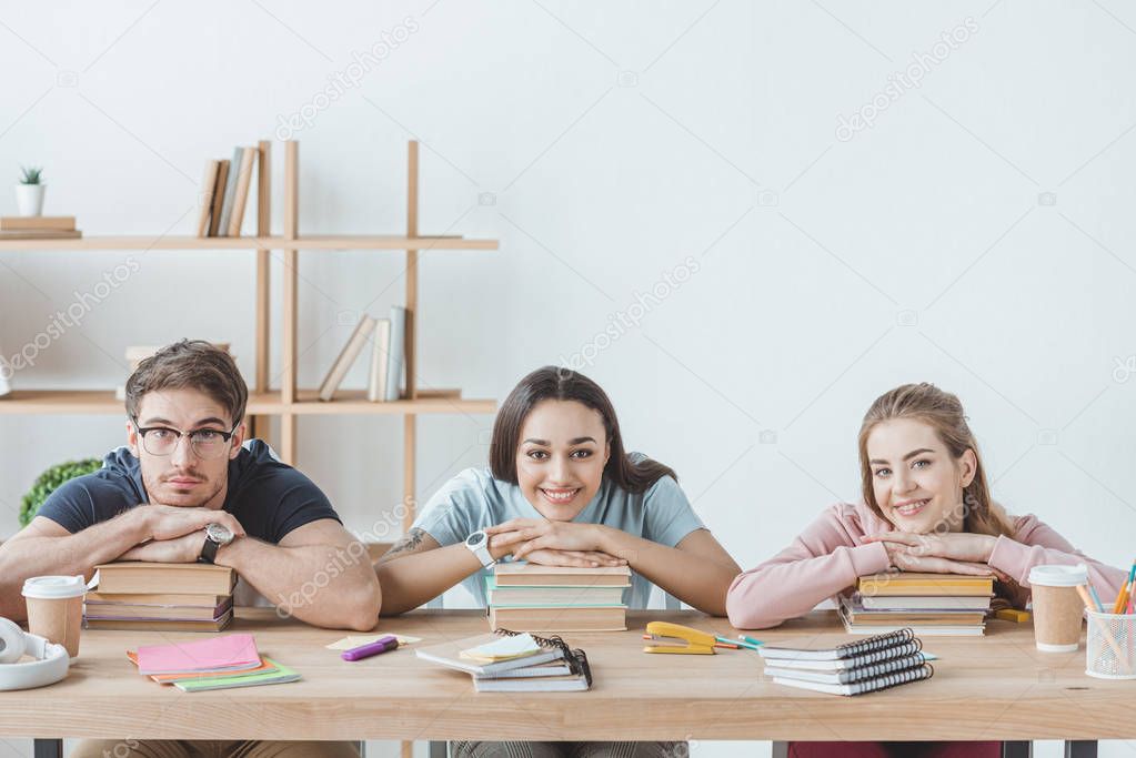 young multicultural students sitting at table with books and copybooks