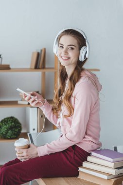 kahve akıllı telefon ve kulaklık ile müzik dinleme ile sarışın öğrenci gülümseyen