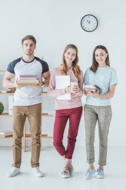 Kitaplar, dizüstü bilgisayar, kahve ve copybooks tutan genç öğrenciler