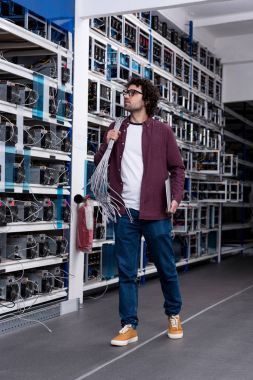 young computer engineer with ethernet wires on shoulder at cryptocurrency mining farm clipart