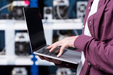 cropped shot of computer engineer working with laptop at cryptocurrency mining farm clipart