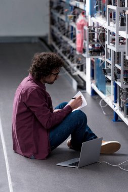 computer engineer working while sitting on floor at cryptocurrency mining farm clipart