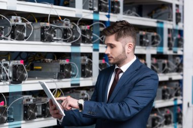 serious young businessman using tablet at ethereum mining farm clipart