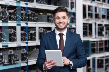 smiling young businessman using tablet at ethereum mining farm clipart